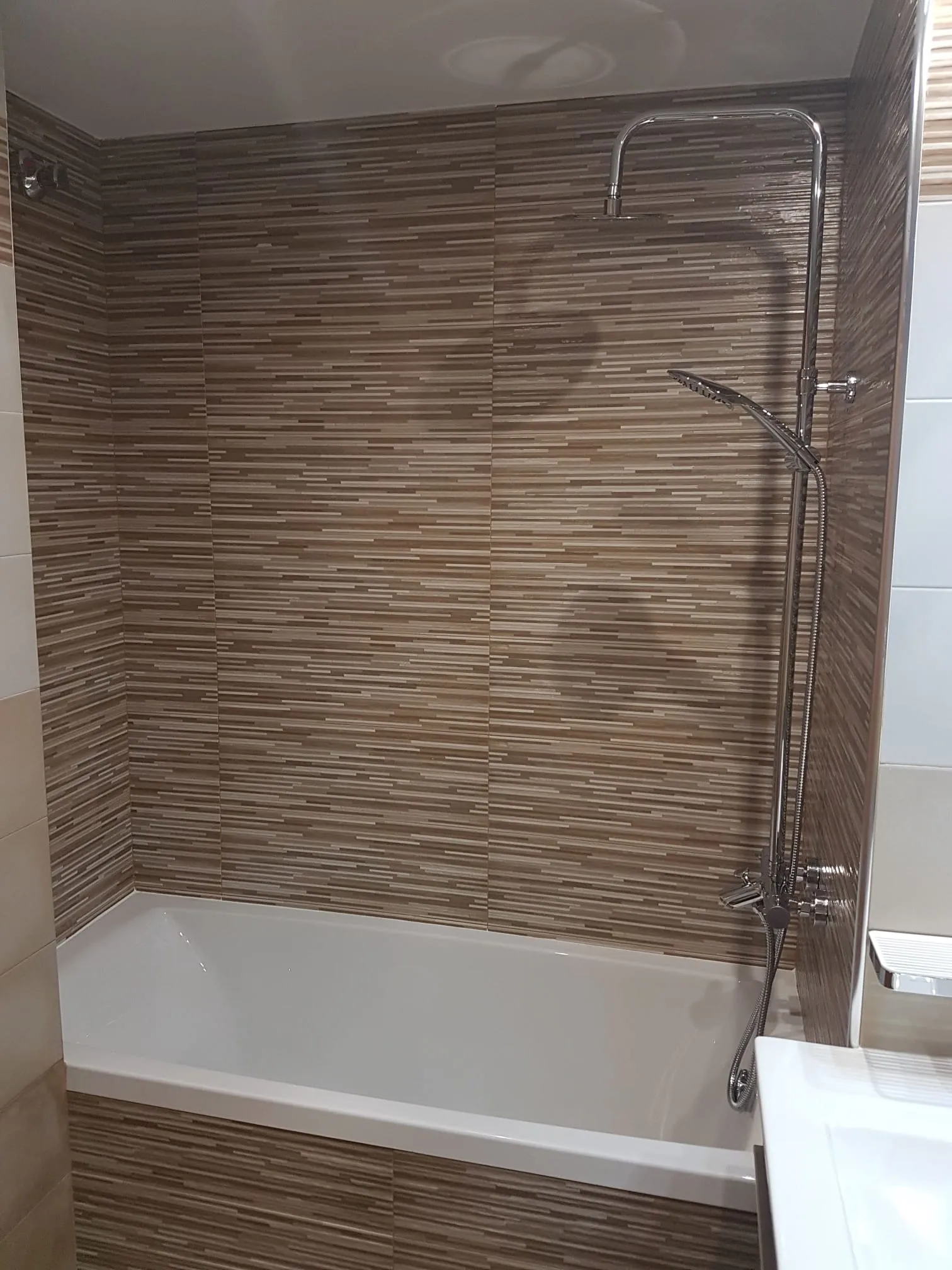 Zona de bañera renovada con columna de ducha y revestimiento cerámico en tonos tierra