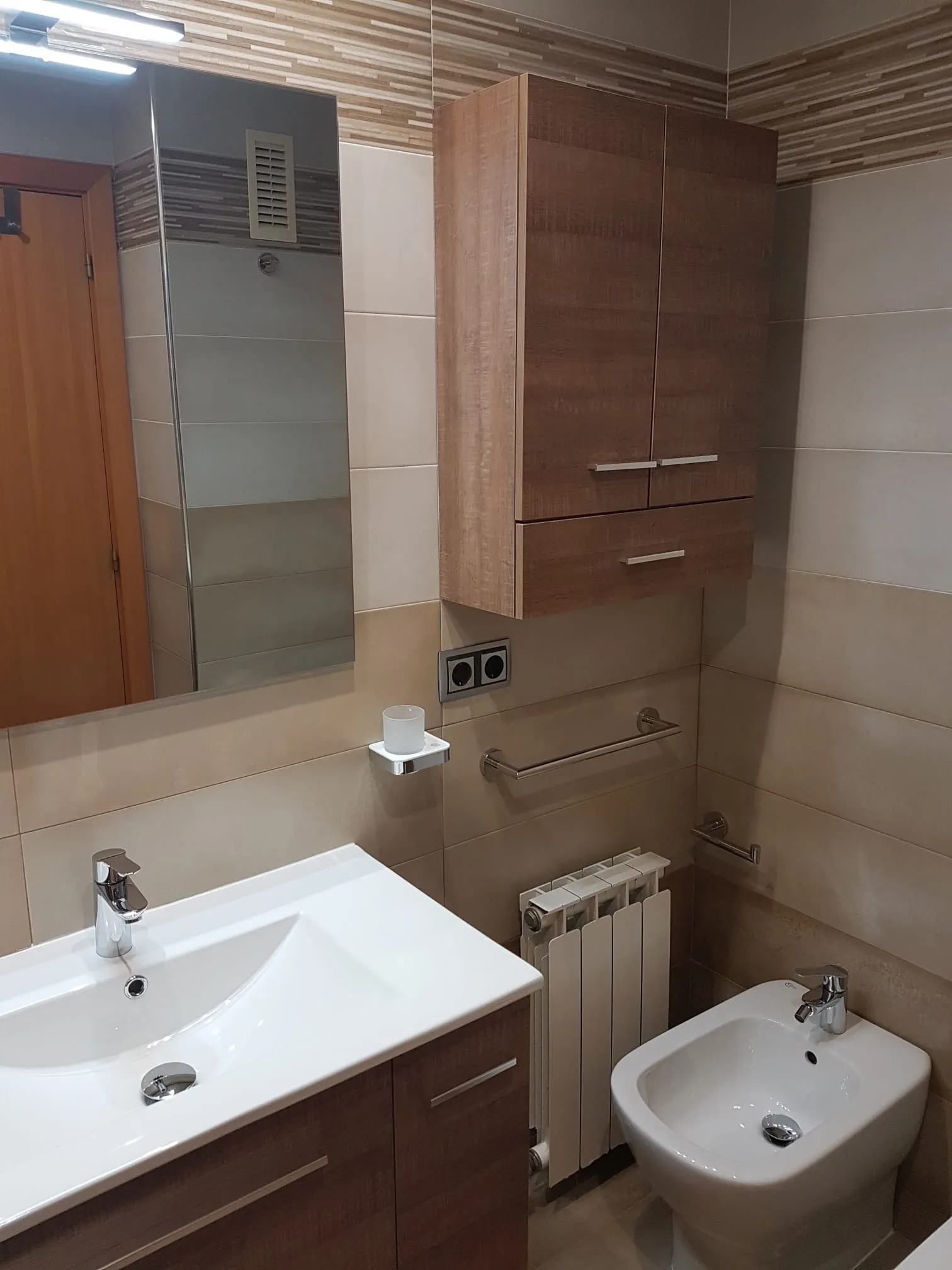 Zona terminada con lavabo, bidé, radiador y muebles de almacenamiento en acabado madera