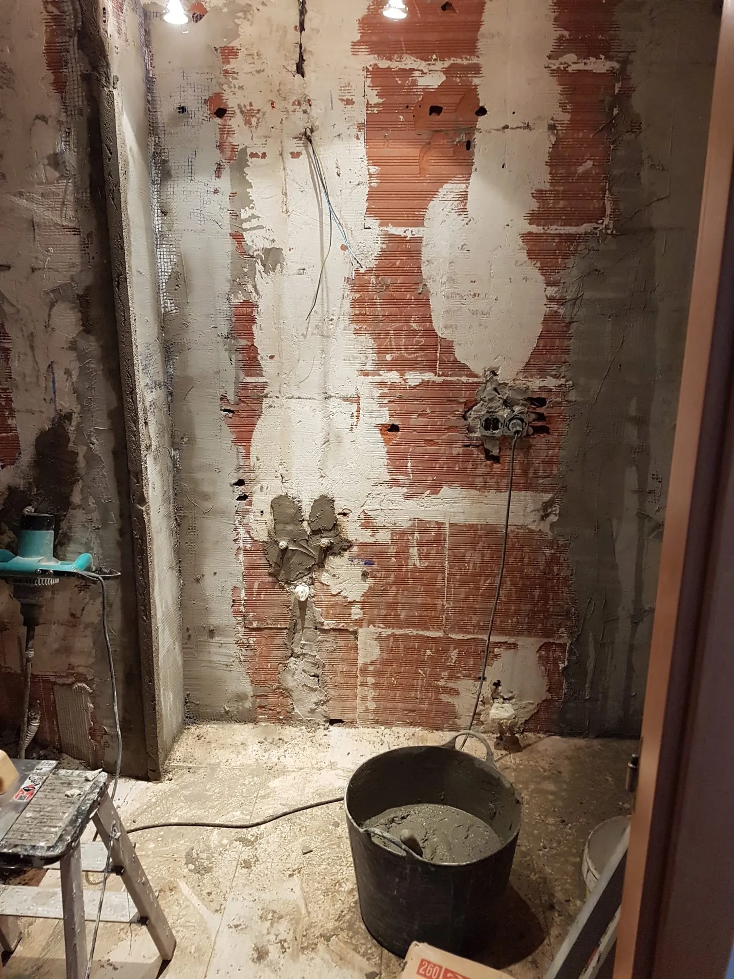 Pared del baño tras retirar los revestimientos, con puntos de fontanería y cableado visibles