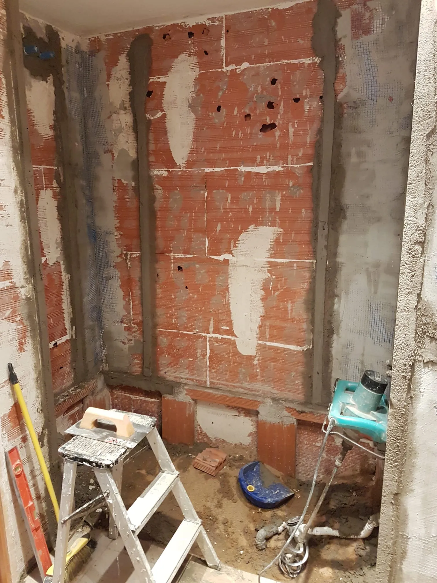 Baño durante la obra, con paredes sin revestimiento, instalaciones vistas y herramientas de trabajo